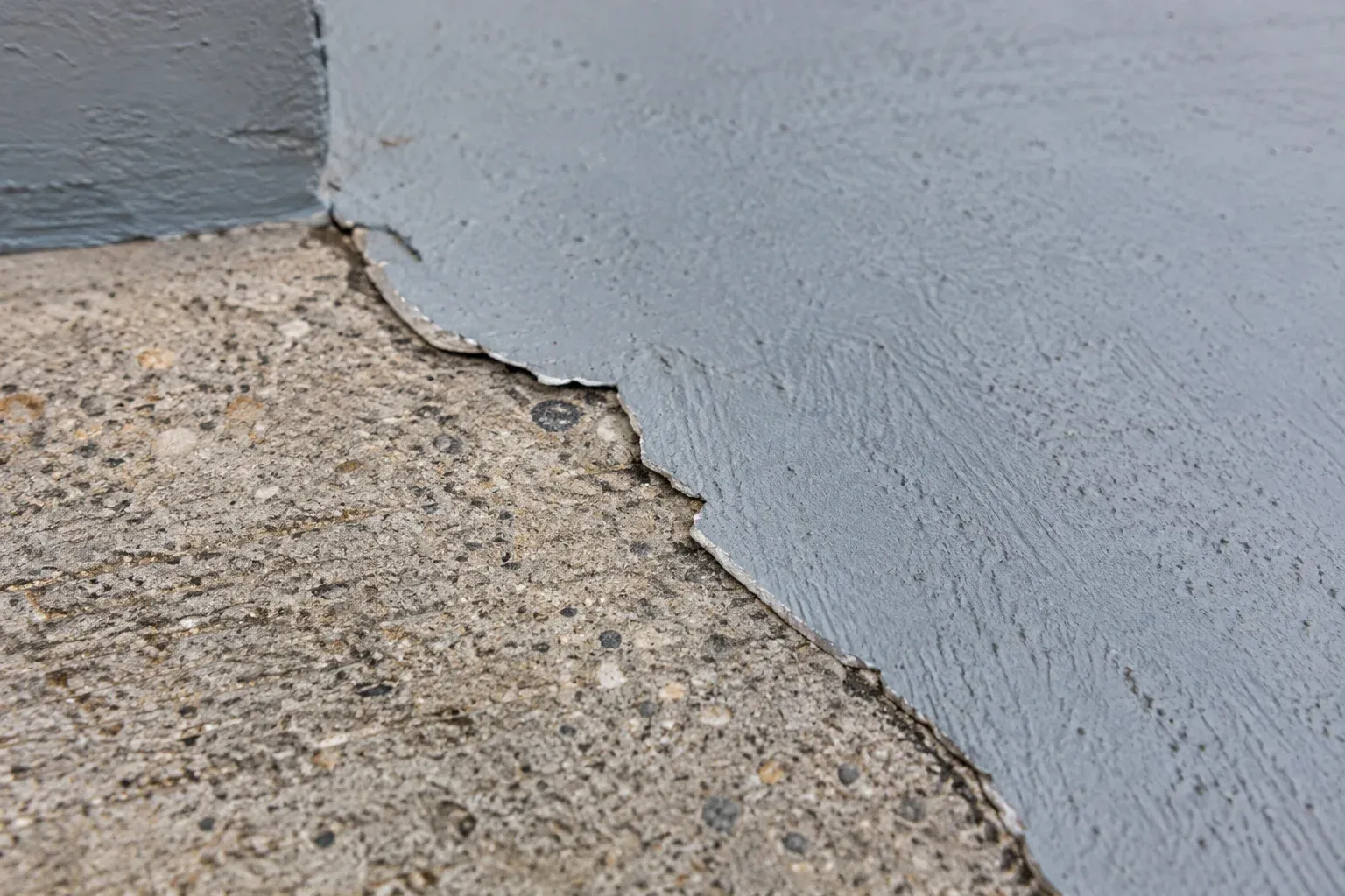 Close view of worn driveway coating showing lifted edges and exposed concrete.